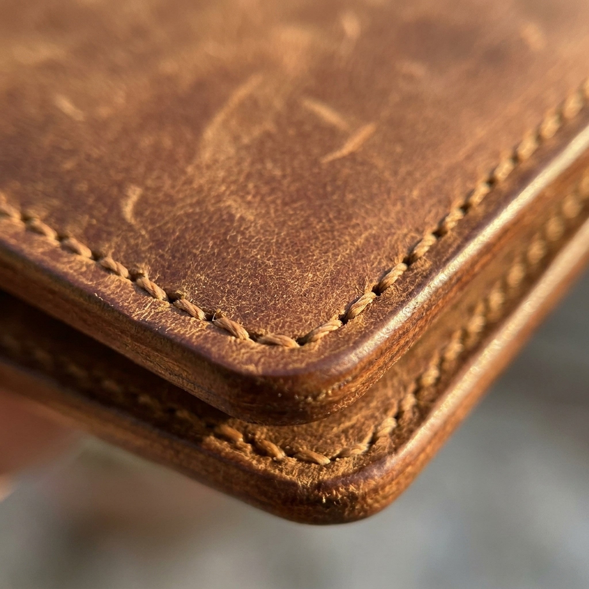 Macro detail of The Drover: the burnished edge, tonal saddle stitching and warm brown Crazy Horse grain
