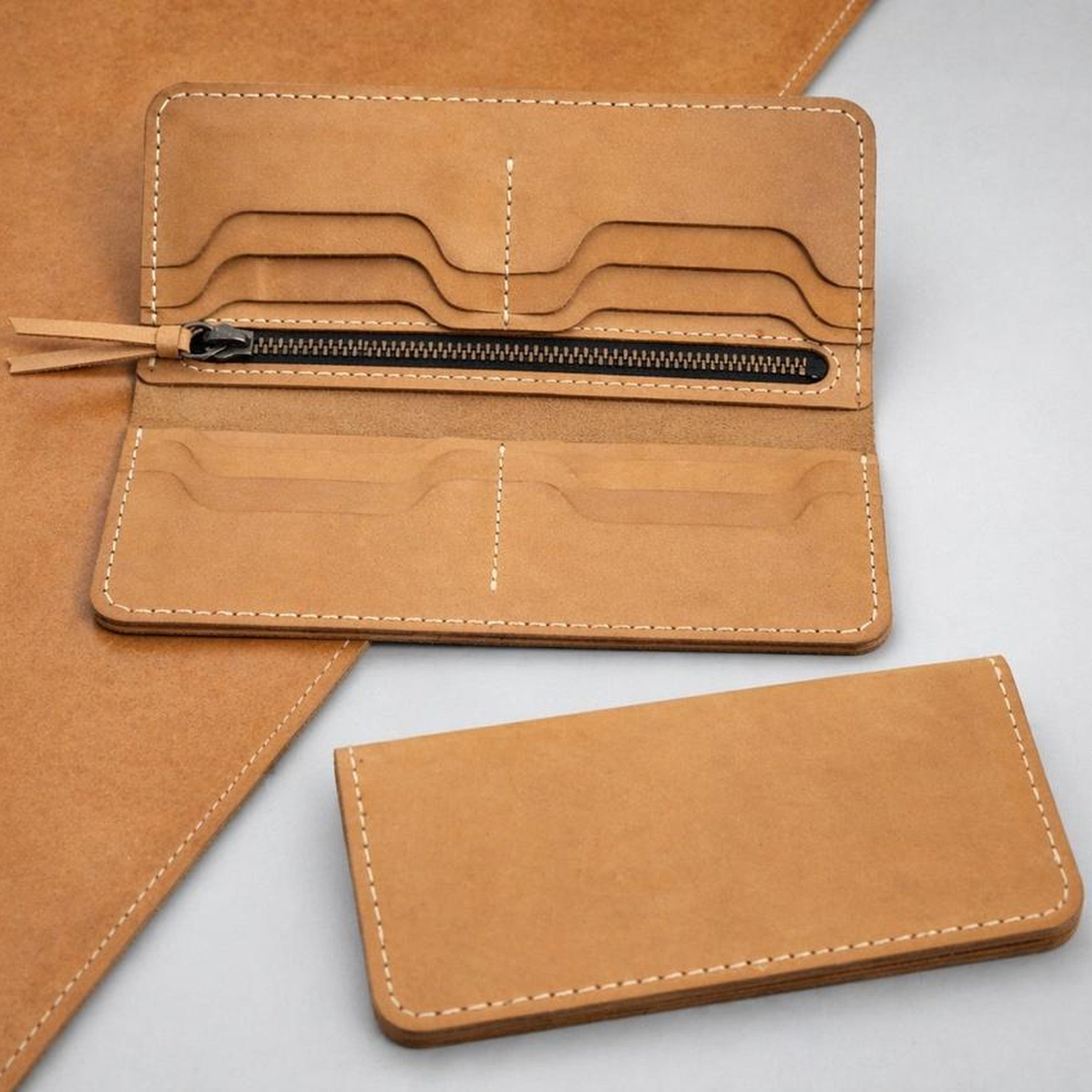 The Ledger long wallet in natural undyed nubuck, shown open with card slots and a zip coin pocket, and closed alongside